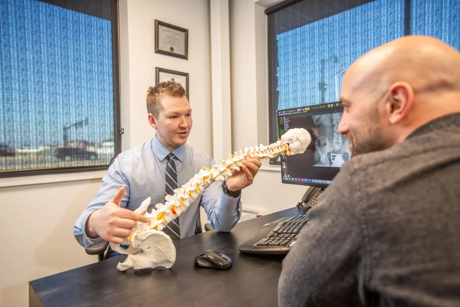 Chiropractor using a spine model to explain an X-ray to a male patient