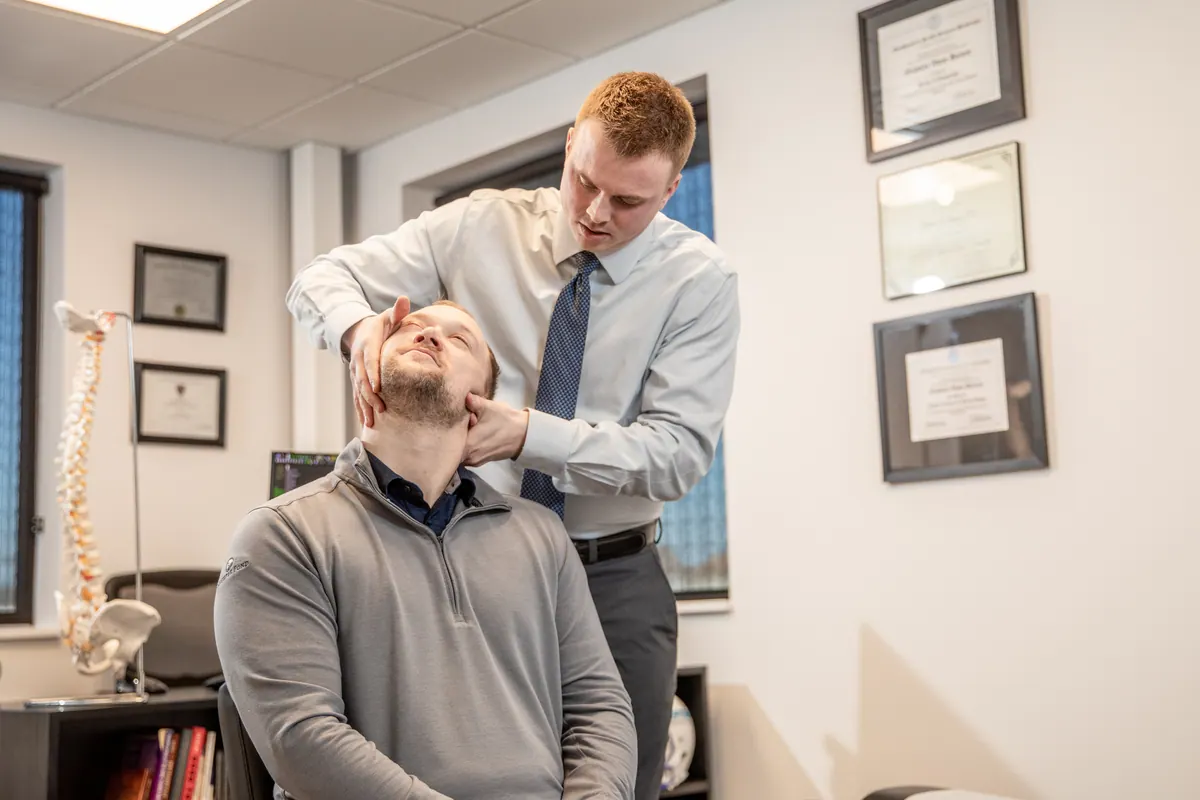 Chiropractor adjusting the neck of a seated male patient