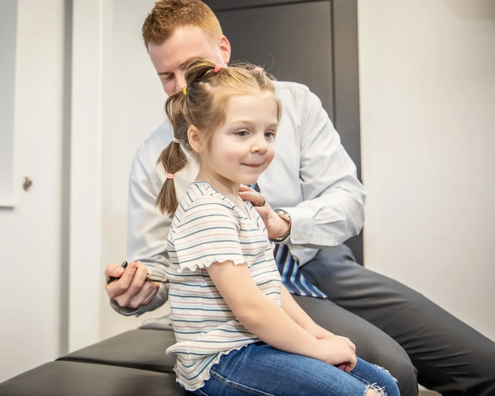 Chiropractor checking a young girl's spine while she sits on a table