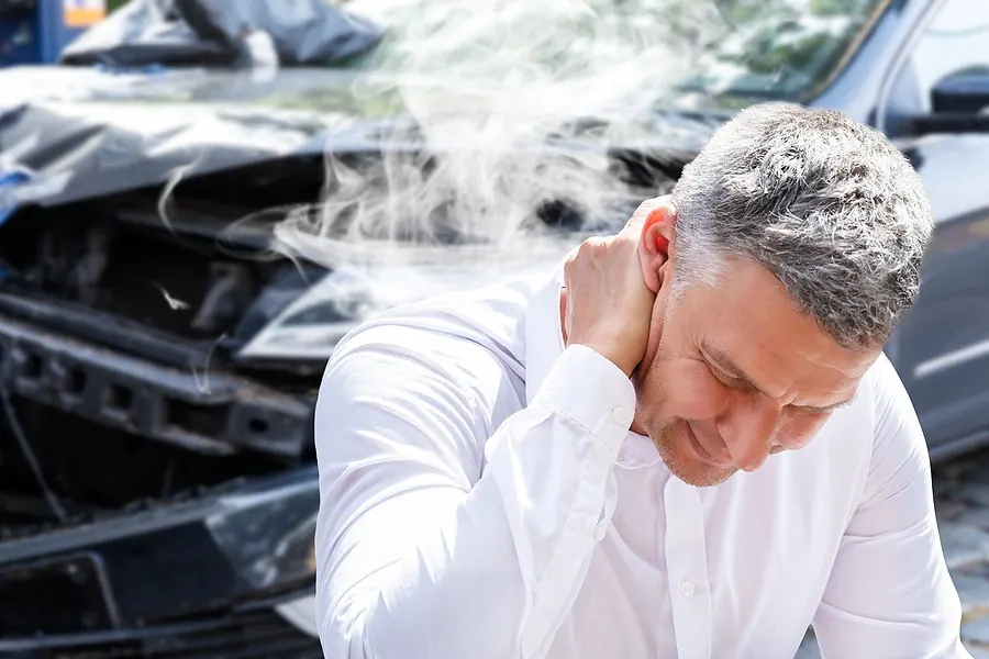 Man holding his neck in front of a damaged car