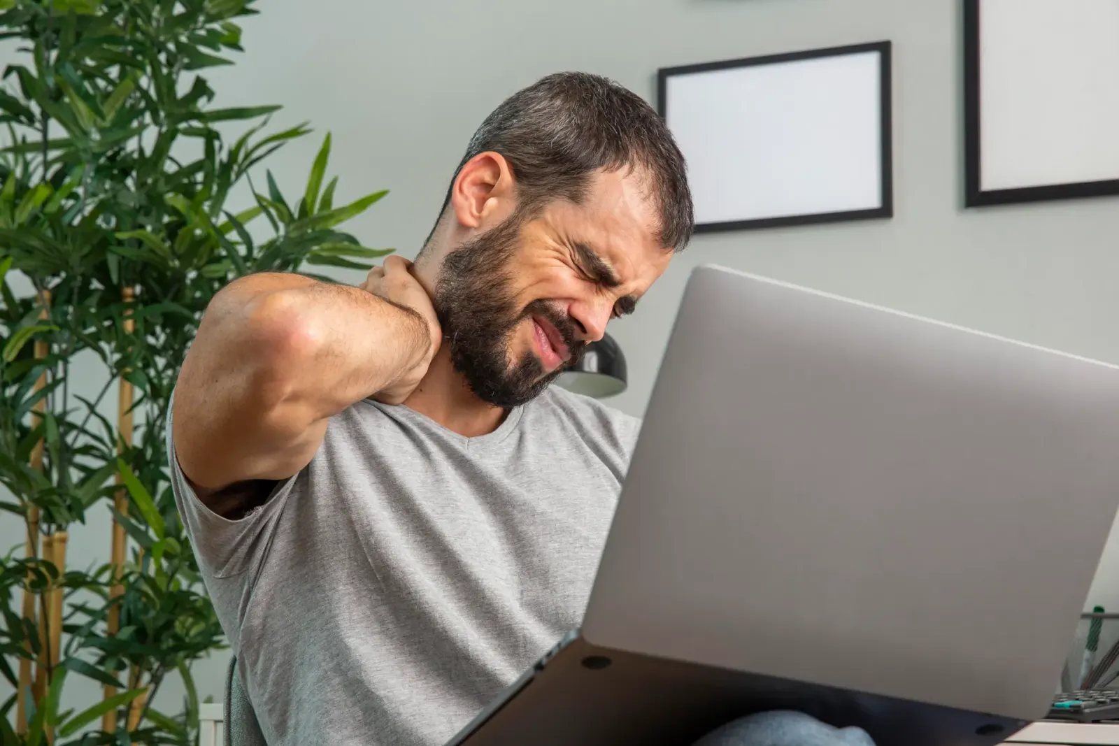 Man at a laptop holding his neck in pain
