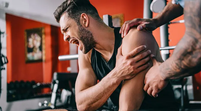 Man at a gym grimacing as someone holds his shoulder