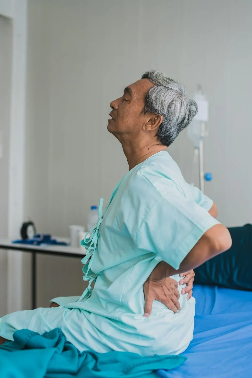 Older man sitting on a bed holding his lower back
