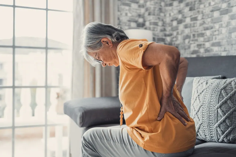 Older man sitting on a sofa holding his lower back