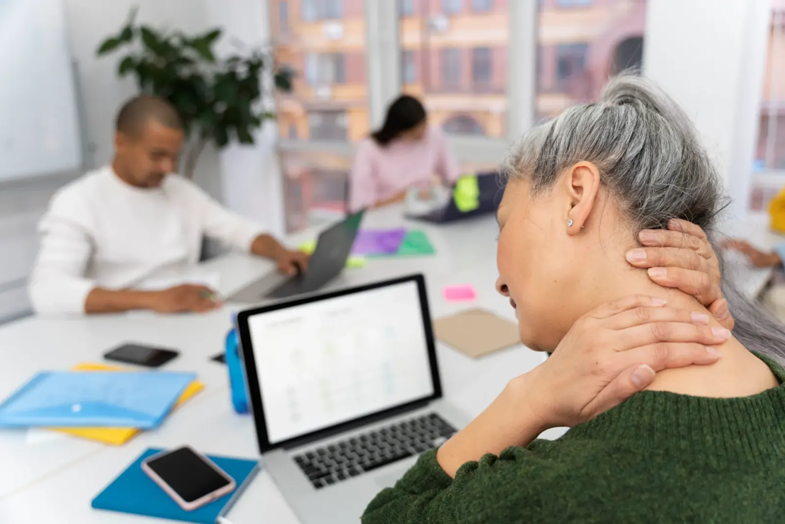Older woman in an office holding the back of her neck