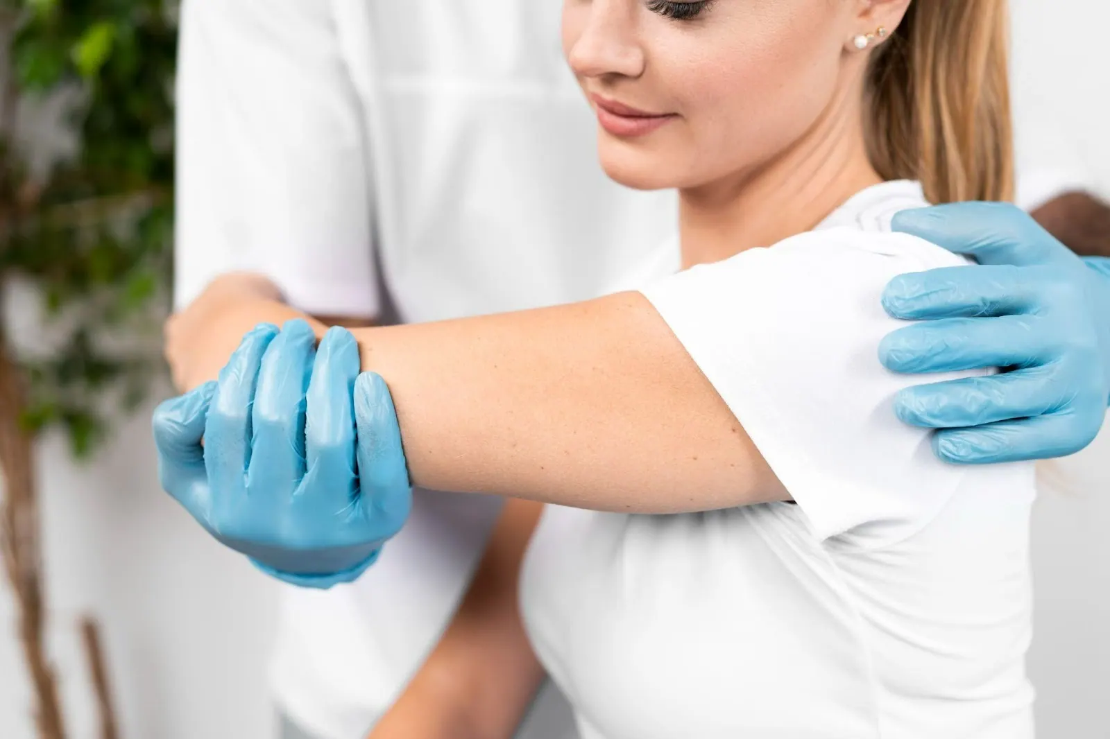 Gloved practitioner examining a woman's shoulder and arm