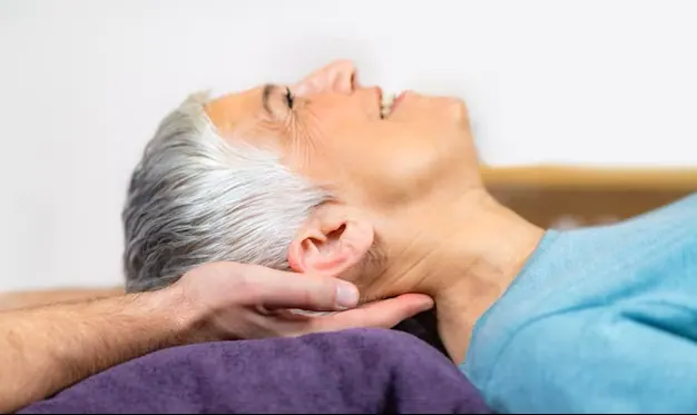 Practitioner supporting an older woman's neck as she lies on a table