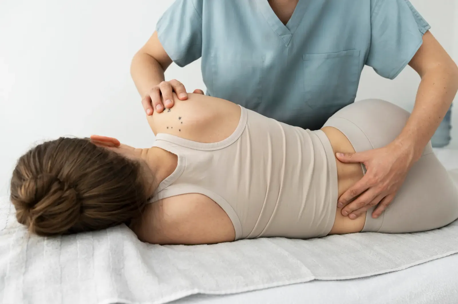 Practitioner treating a patient's lower back as she lies on her side