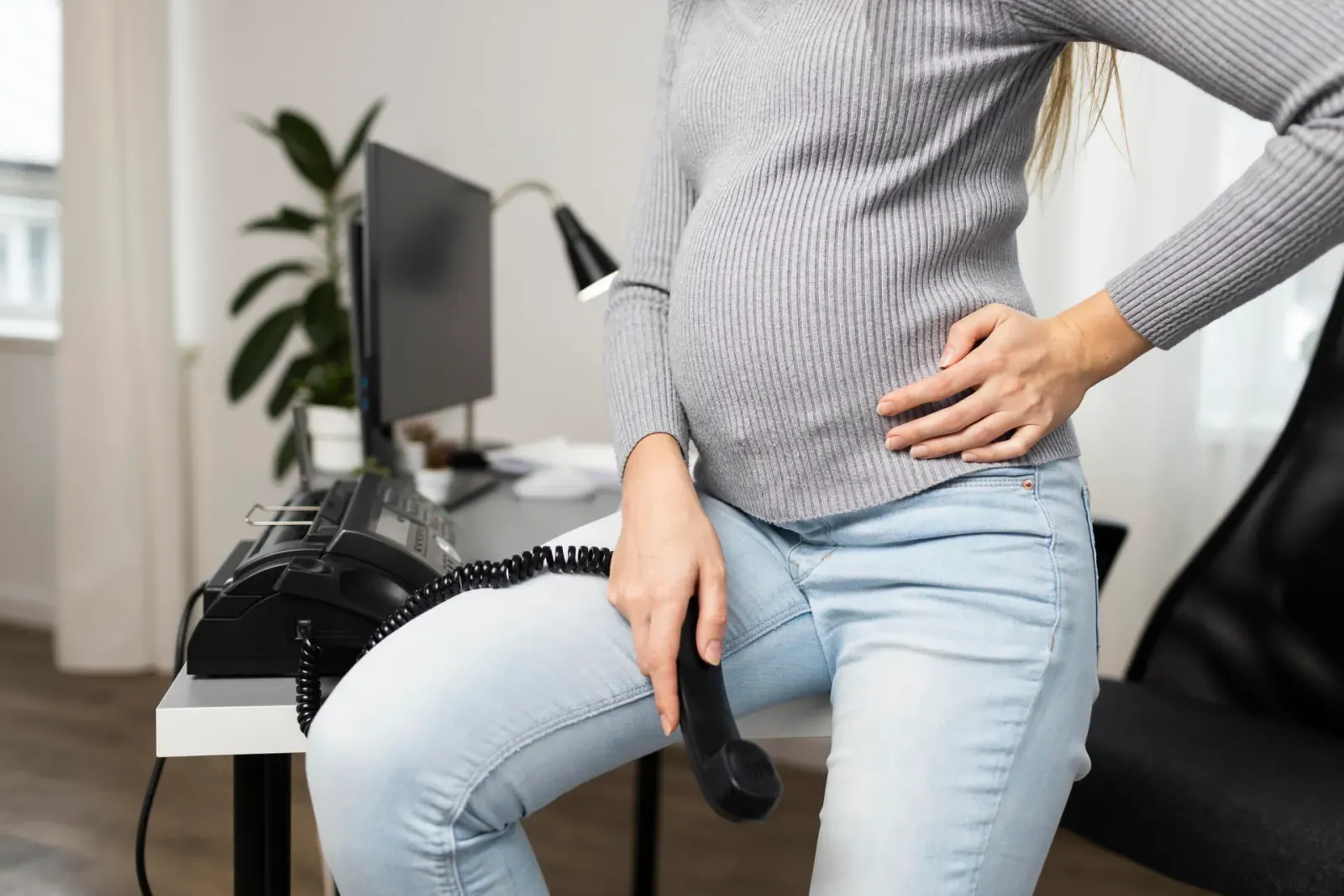 Pregnant woman at a desk resting a hand on her lower back