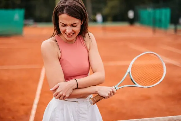 Tennis player holding her elbow on a clay court