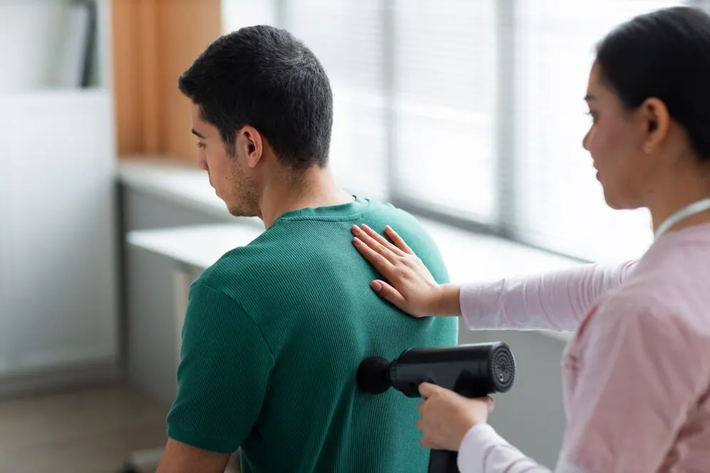Therapist using a massage gun on a patient's upper back