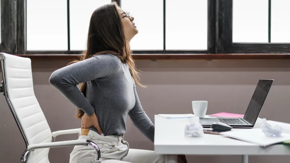 Woman stretching her sore back while working at a desk at home