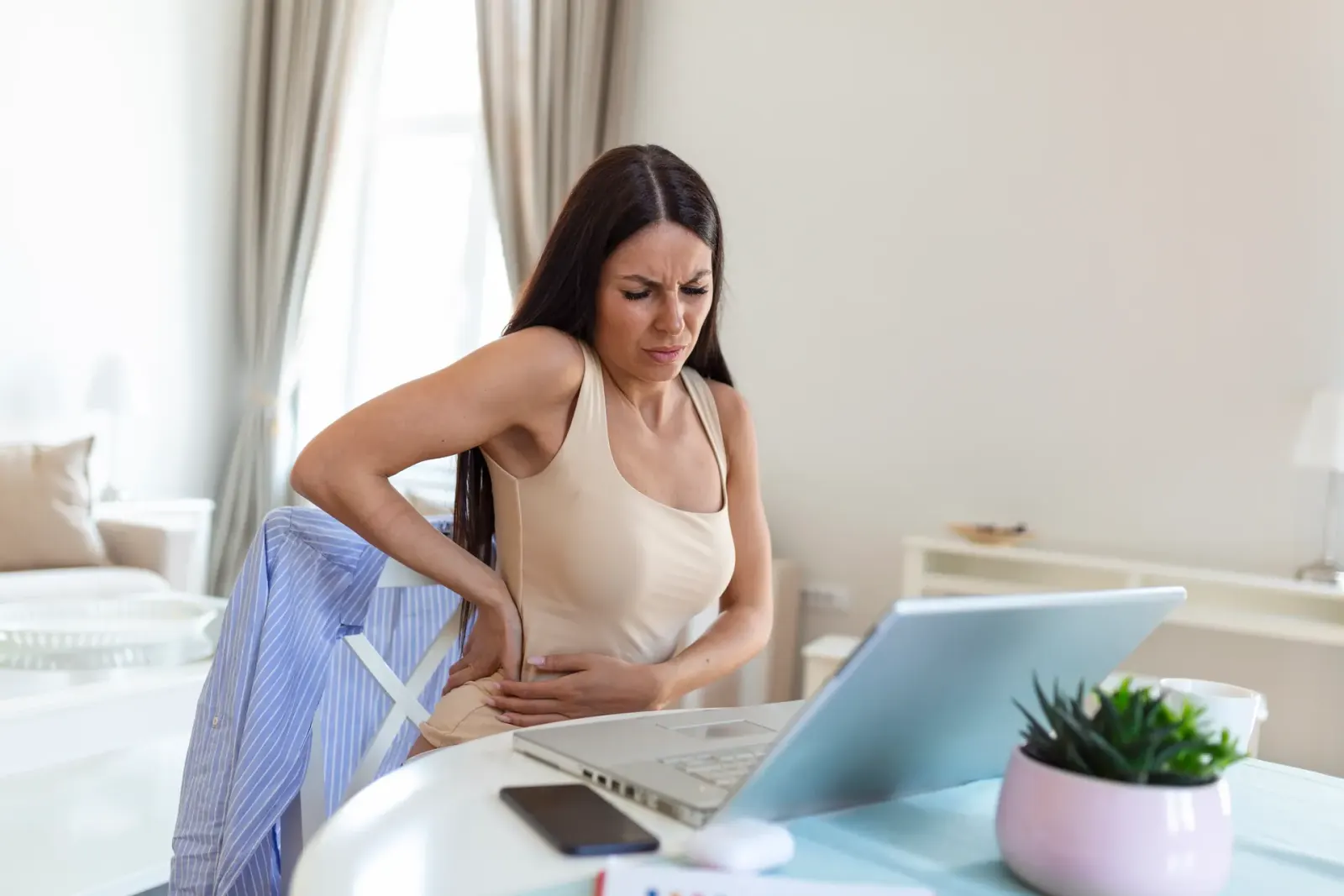 Woman at a laptop holding her lower back