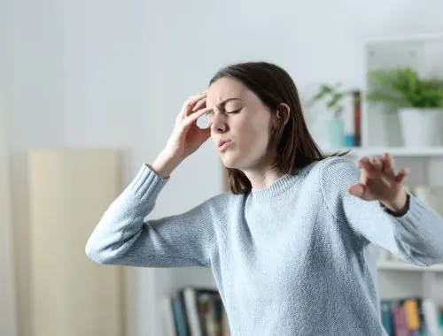 Woman holding her head and reaching out to steady herself