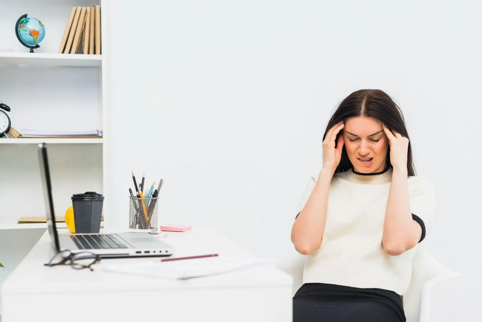 Woman at a home desk holding her head