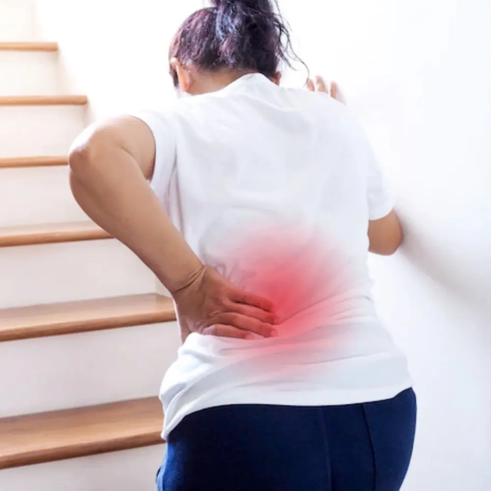 Woman on a staircase holding her lower back with the painful area highlighted