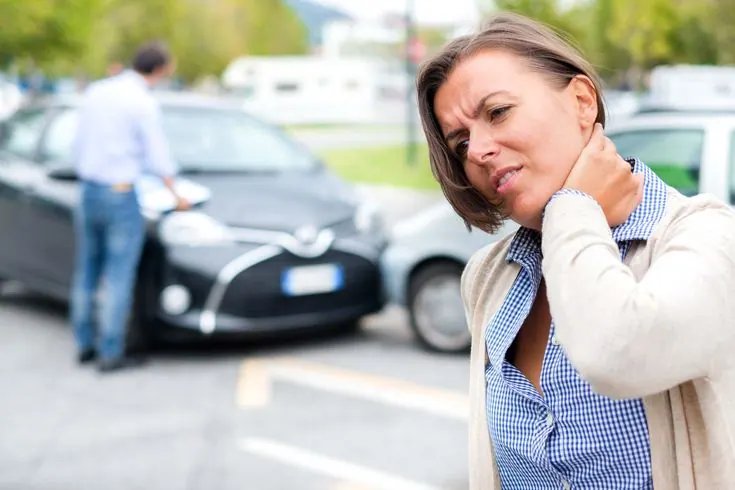 Woman holding her neck after a car accident with damaged cars behind her