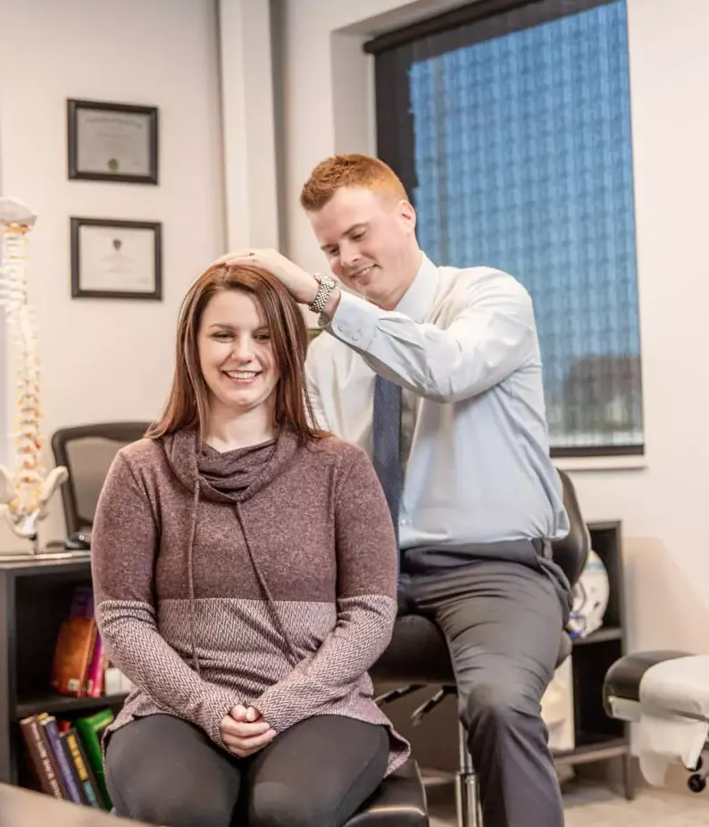 Chiropractor adjusting the neck of a smiling seated patient