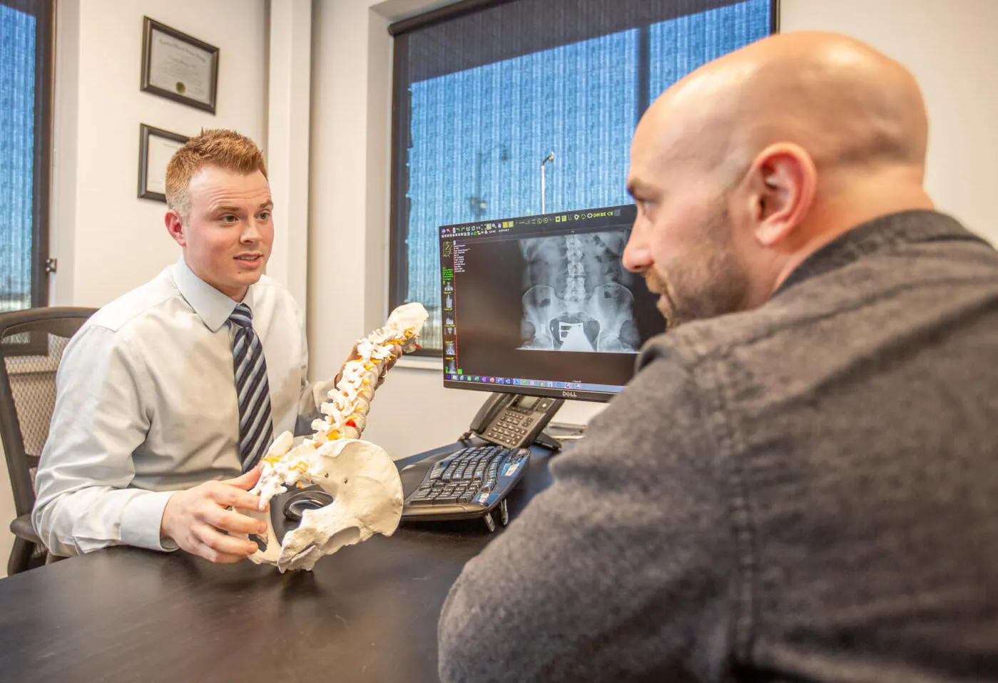 Chiropractor using a spine model to explain an X-ray to a male patient