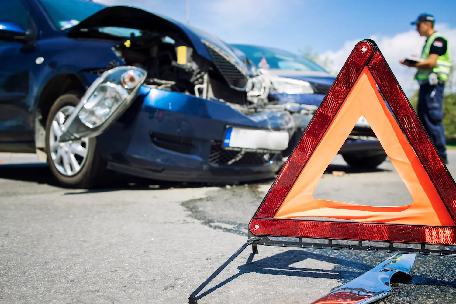 Damaged car behind a red warning triangle with a police officer in the background