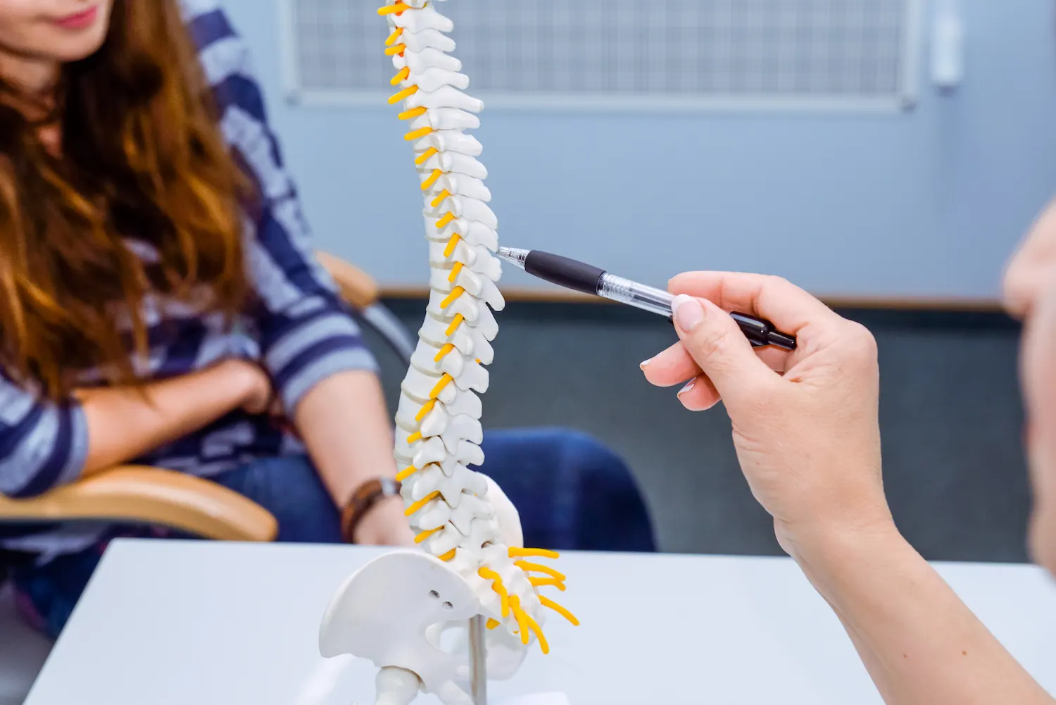 Practitioner pointing a pen at a spine model while talking with a patient