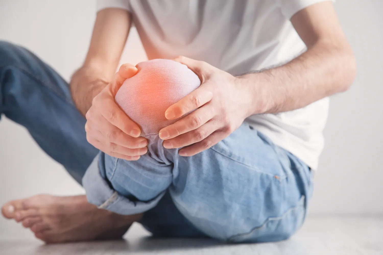 Man sitting on the floor holding his knee with the painful area highlighted