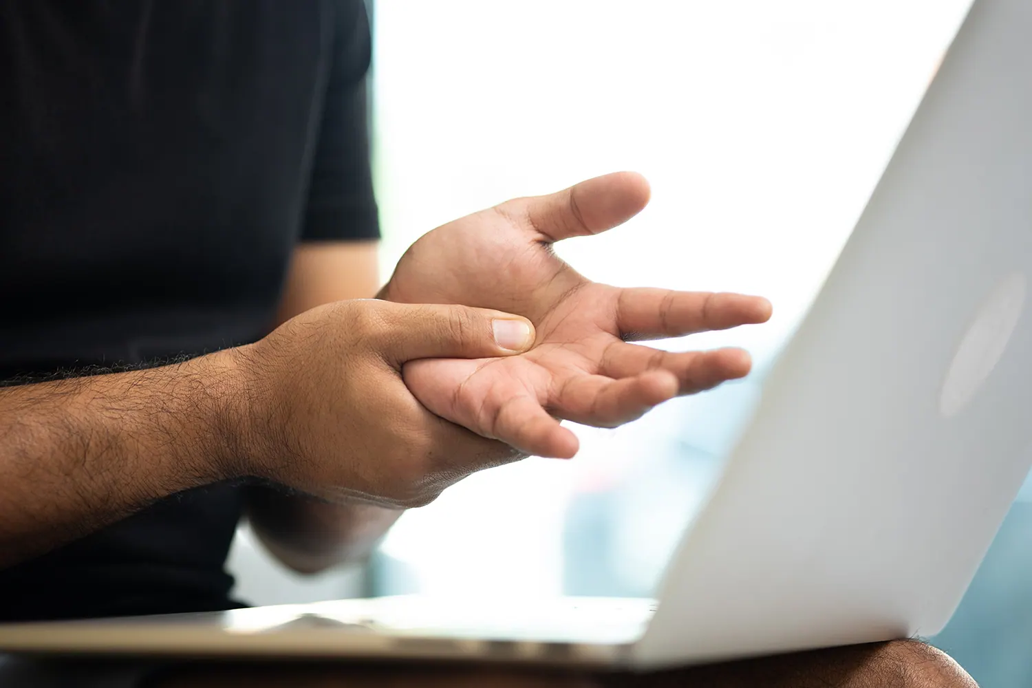 Man holding his wrist while using a laptop