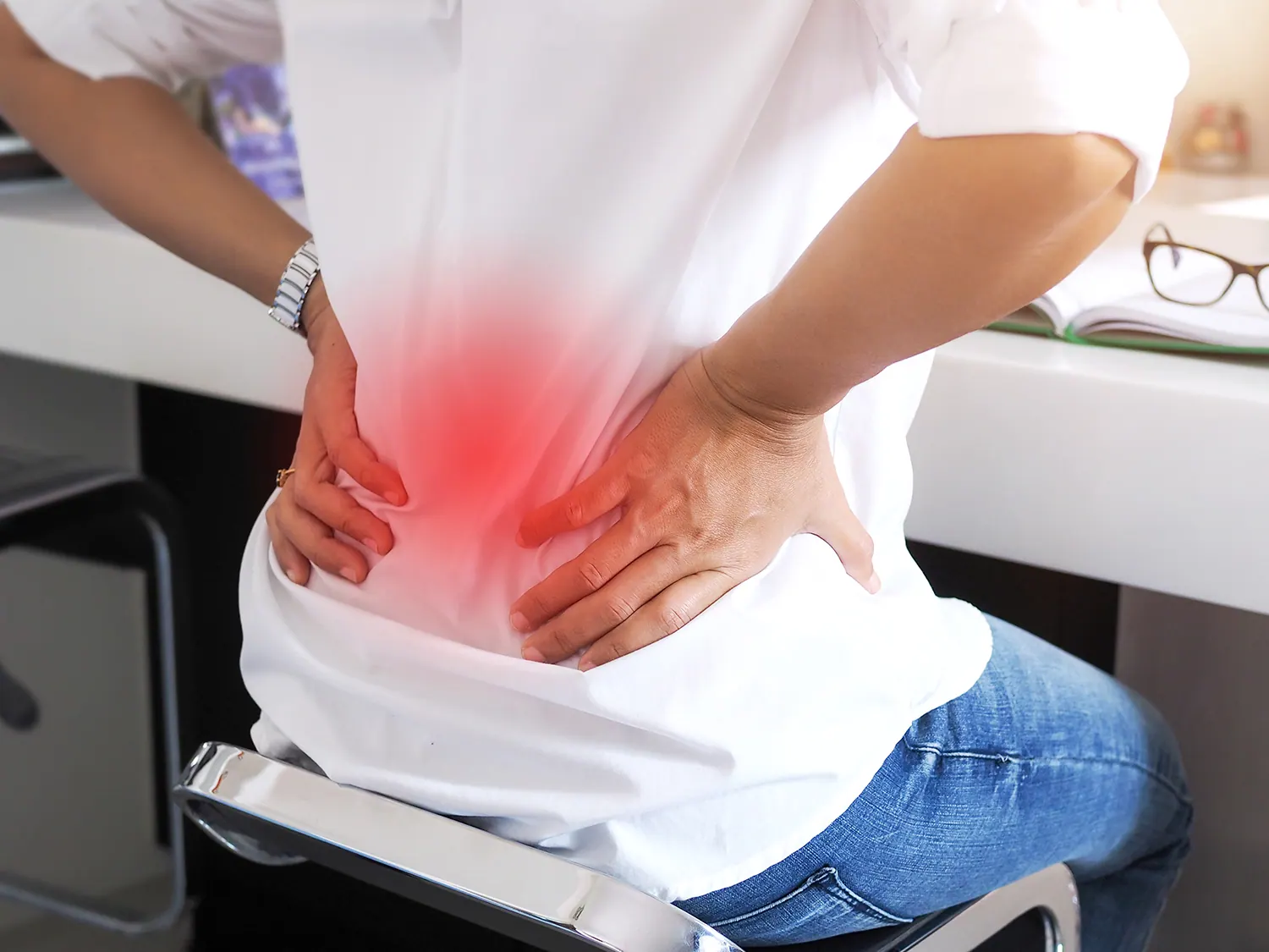 Person at a desk holding their lower back with the painful area highlighted in red