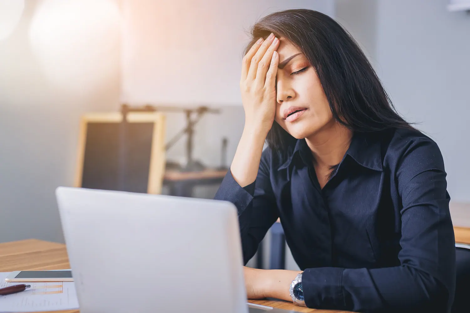 Woman at a laptop holding her forehead