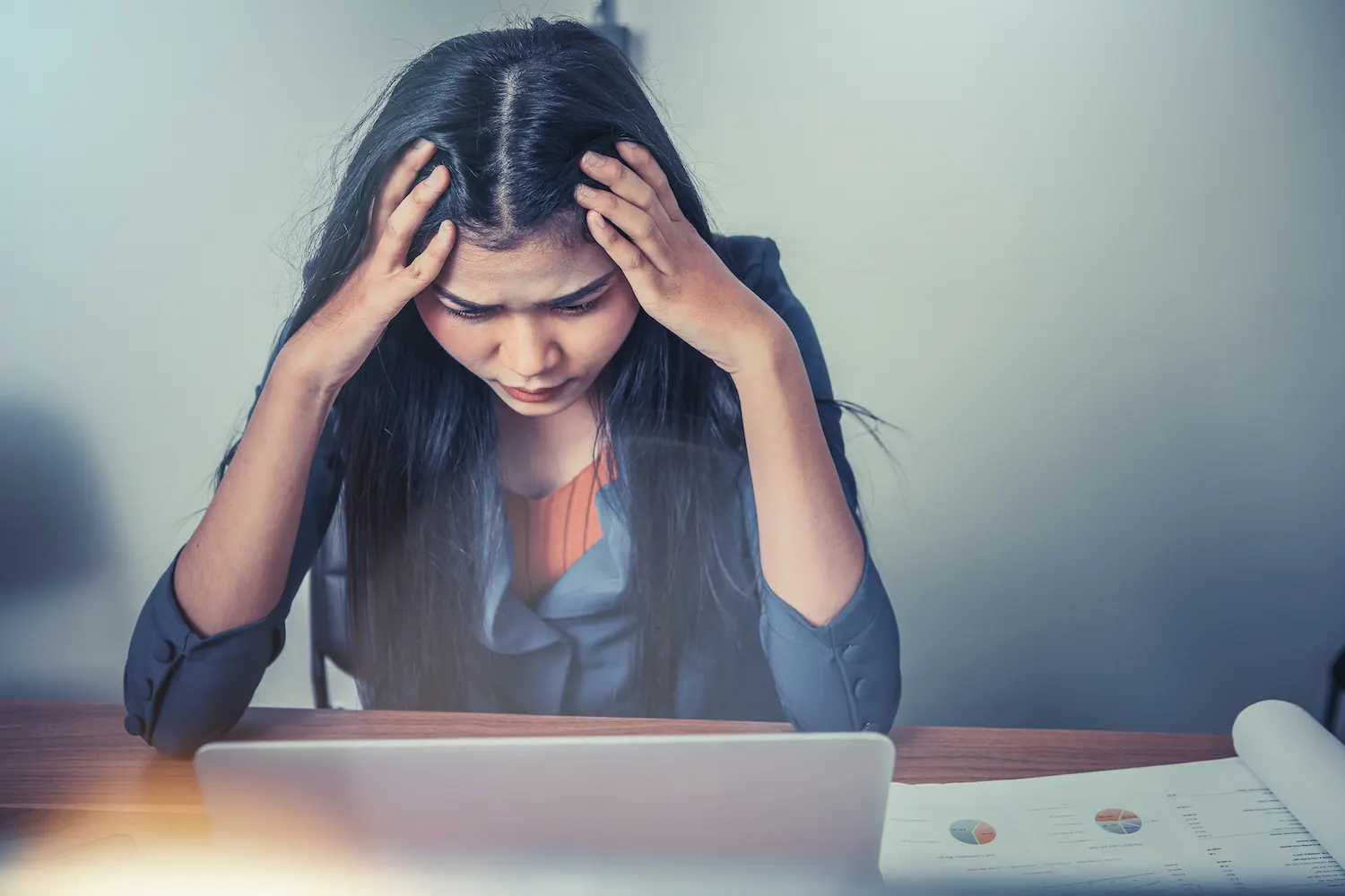 Woman at a desk holding her head with both hands
