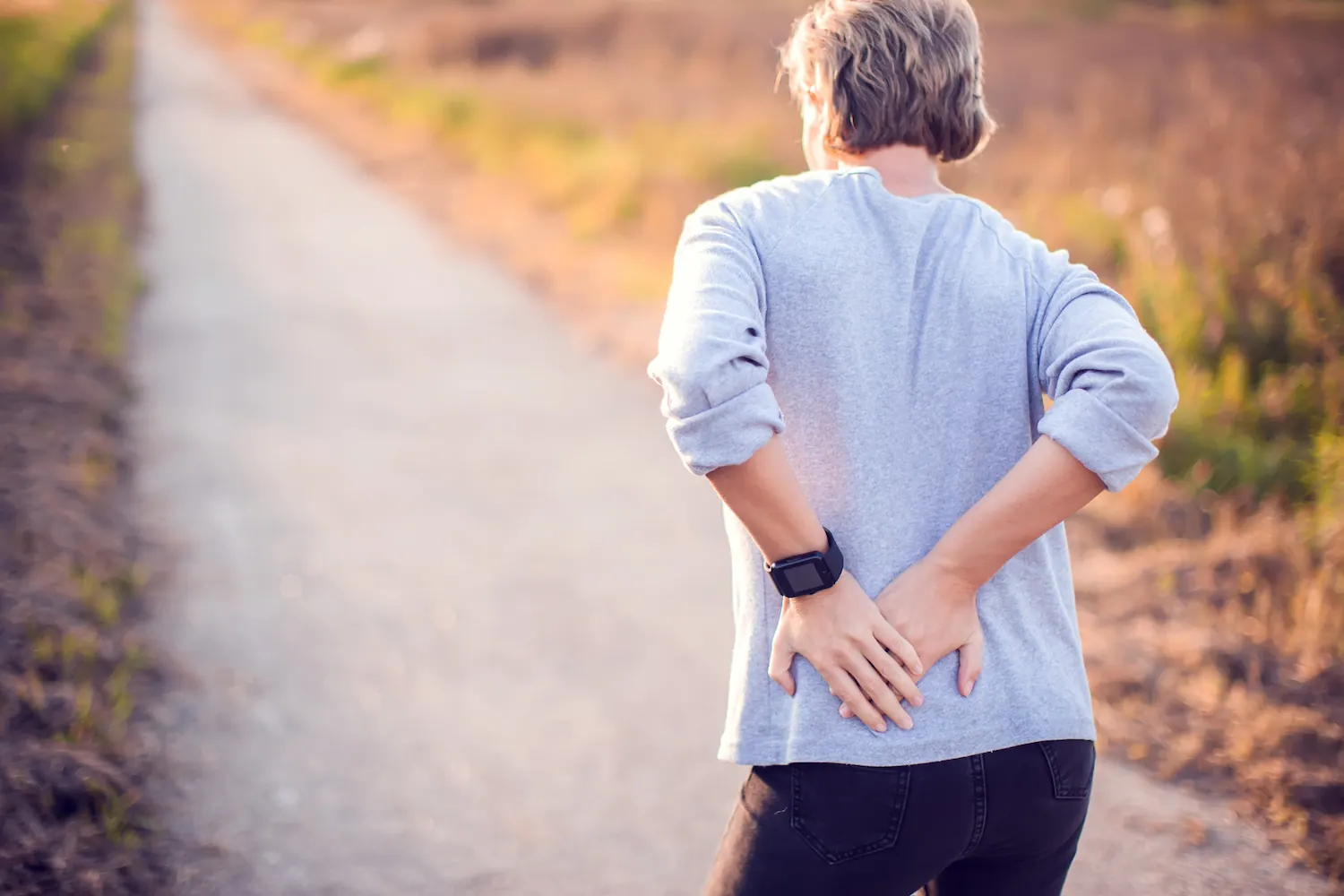Older woman on a walking path holding her lower back and hip