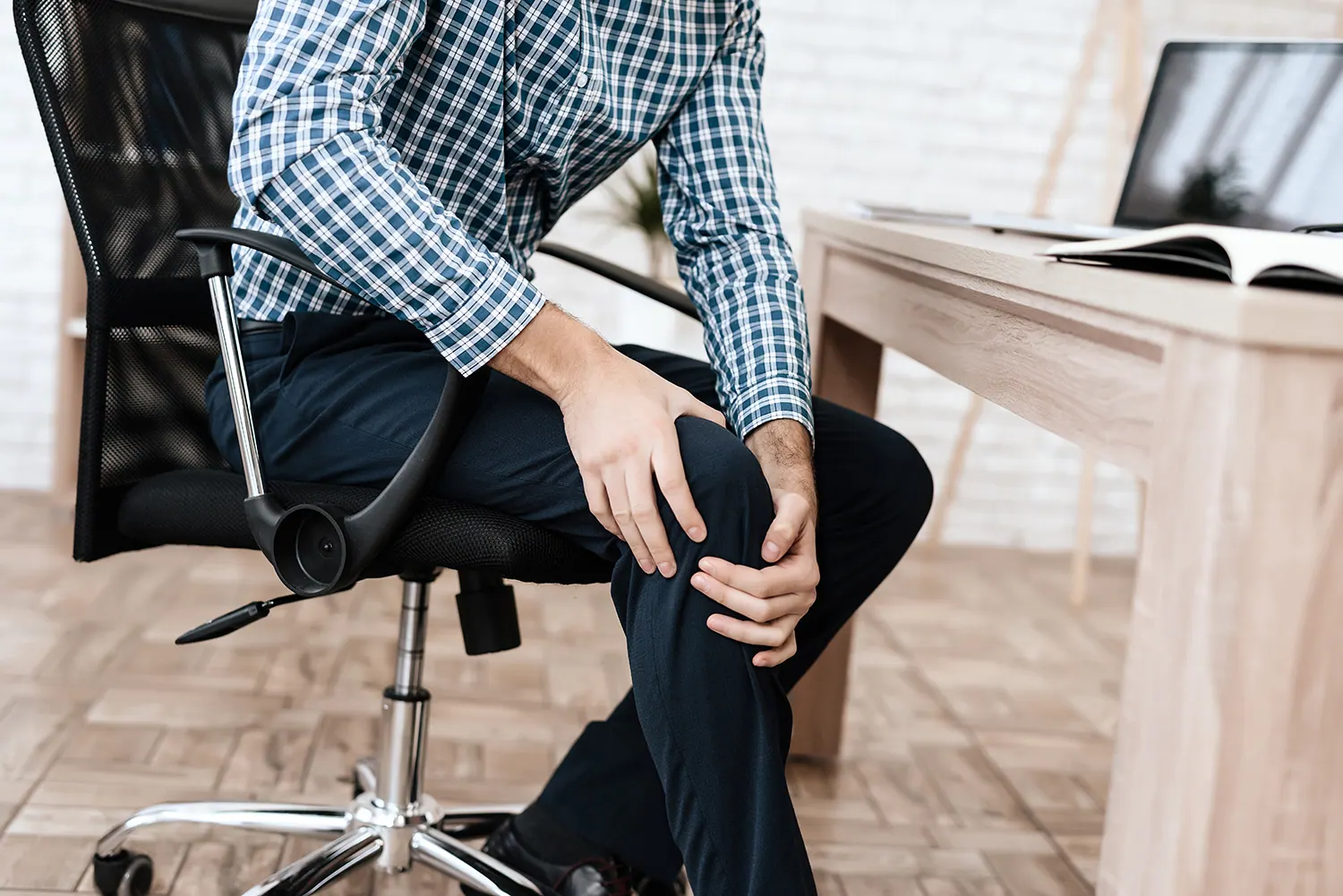 Man sitting in an office chair holding his knee