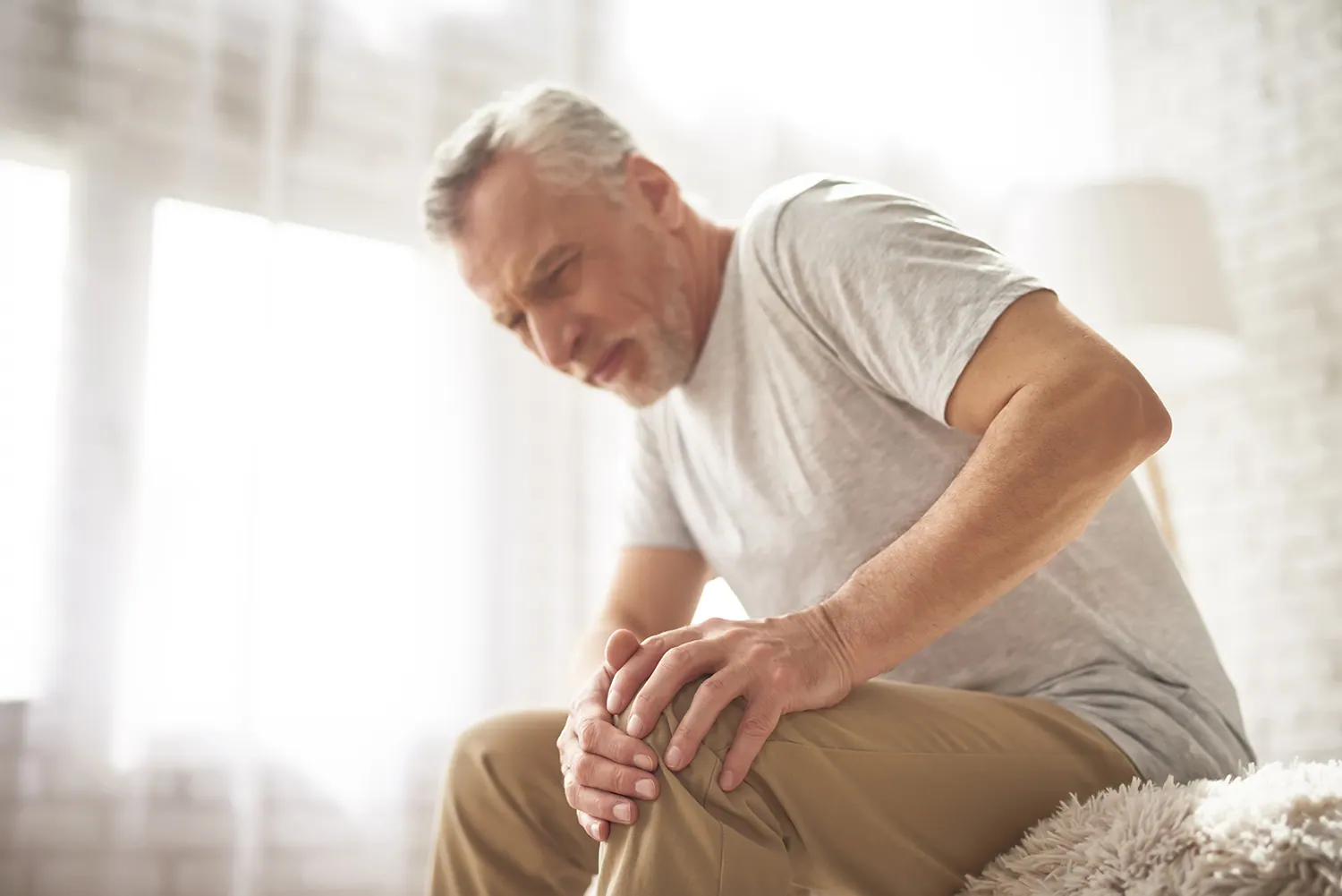 Older man sitting and holding his knee in pain
