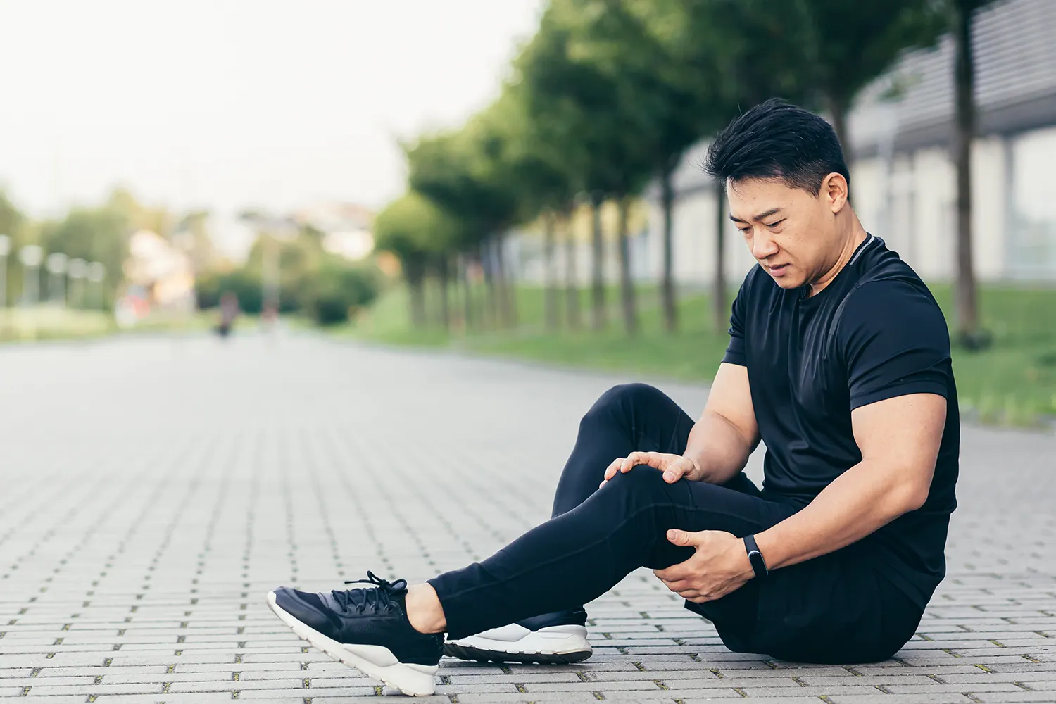 Man sitting on a paved path holding his leg