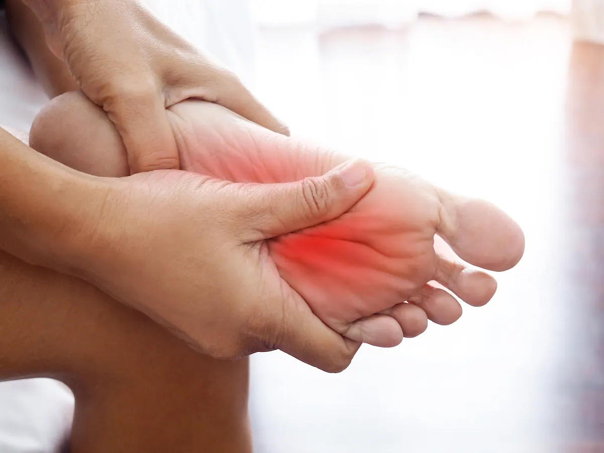 Hands holding a foot with arch pain highlighted in red