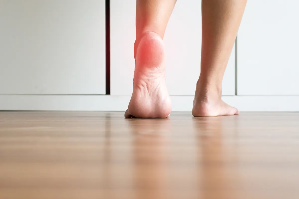 Bare feet on a wooden floor with heel pain highlighted in red