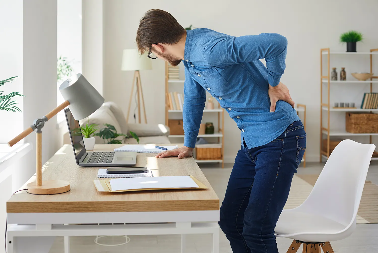 Man bending over a desk holding his lower back