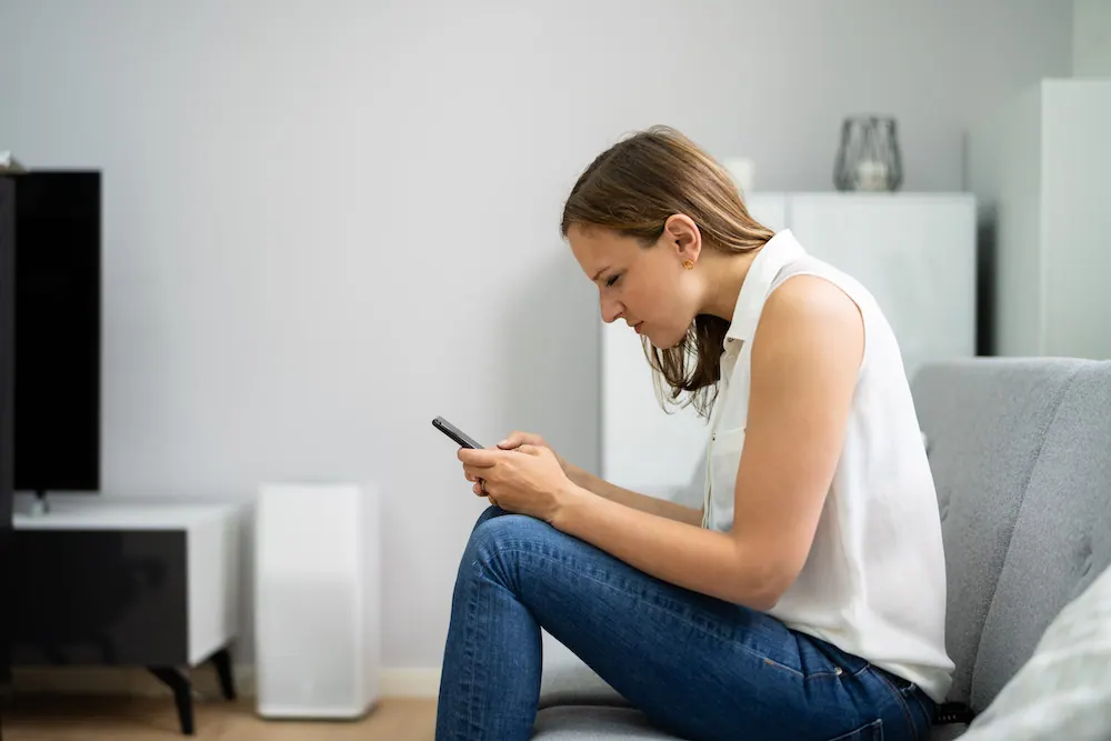 Woman hunched over her phone while sitting on a sofa