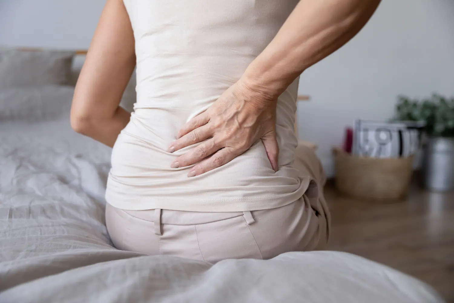 Woman sitting on a bed holding her lower back