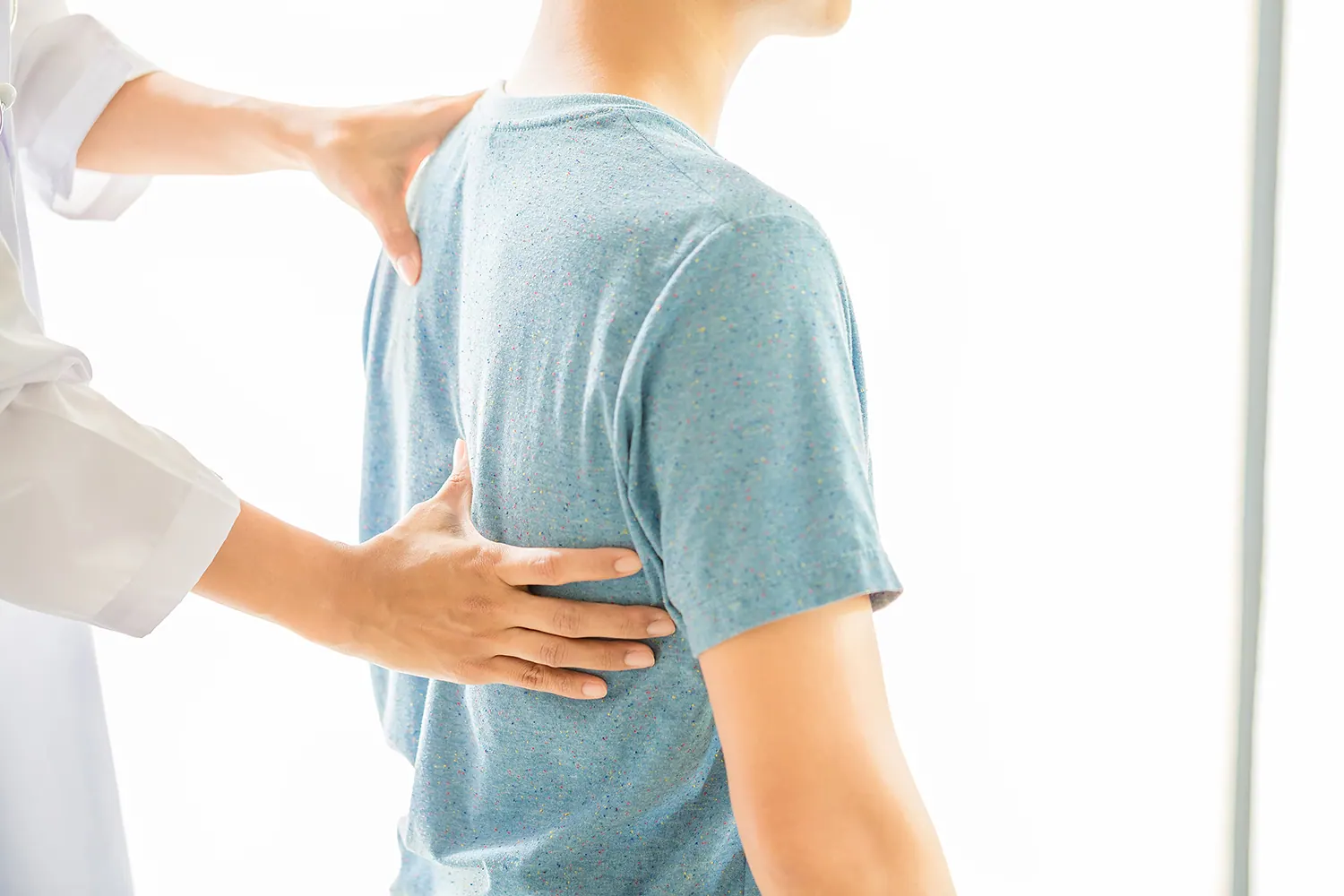 Practitioner placing hands on a young man's back to check alignment