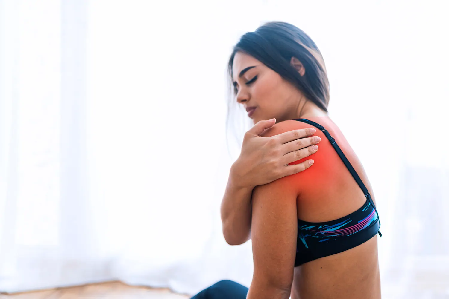 Woman holding her shoulder with the painful area highlighted in red