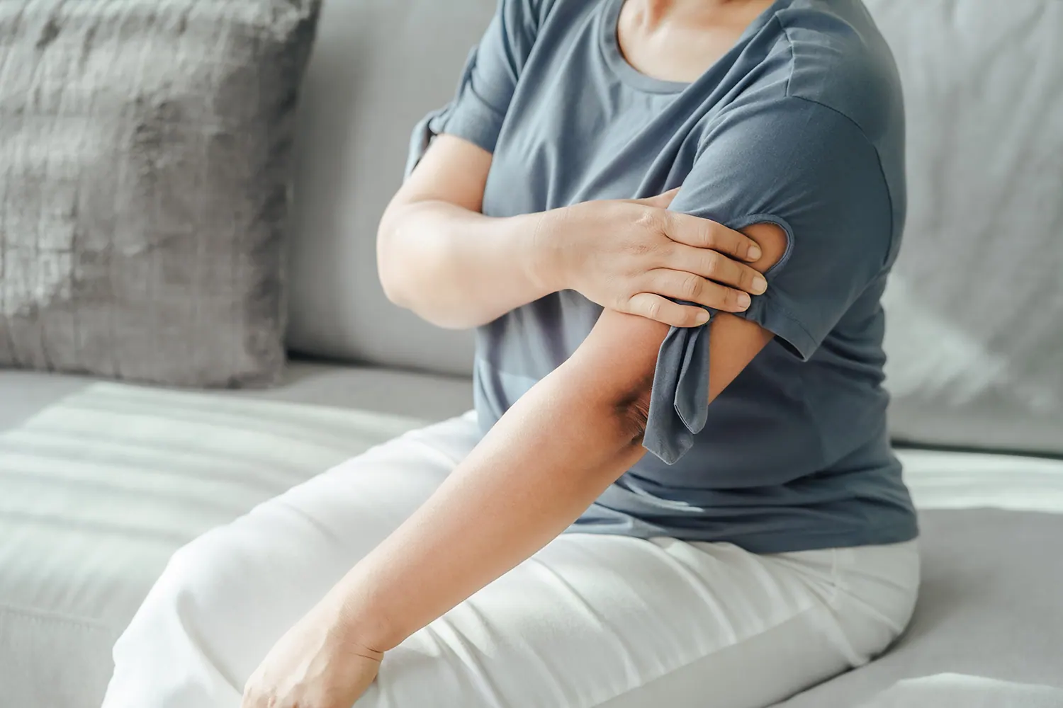 Woman sitting on a sofa holding her shoulder