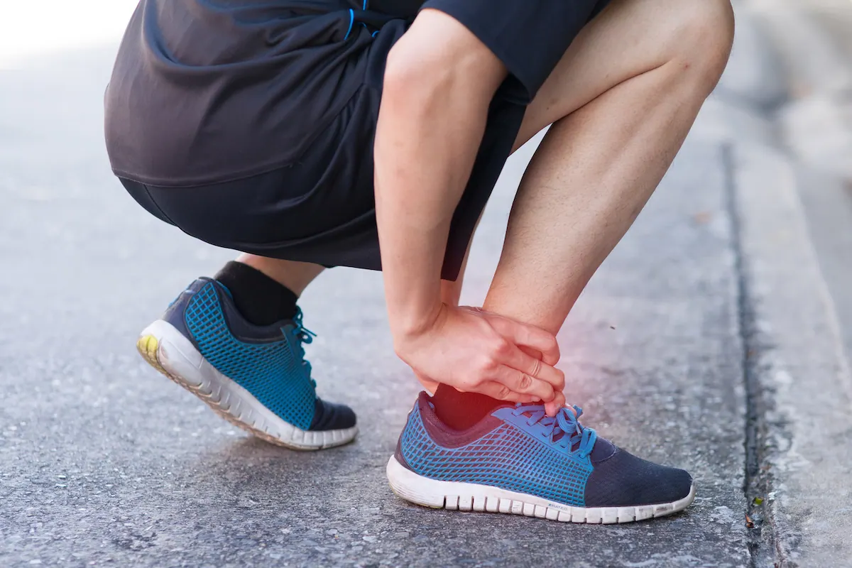 Runner crouching and holding his ankle with the painful area highlighted