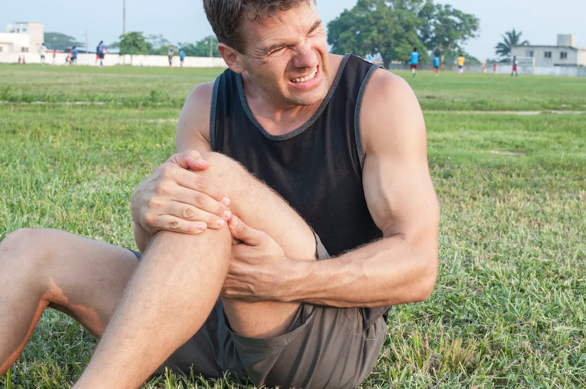 Man sitting on grass holding his knee in pain