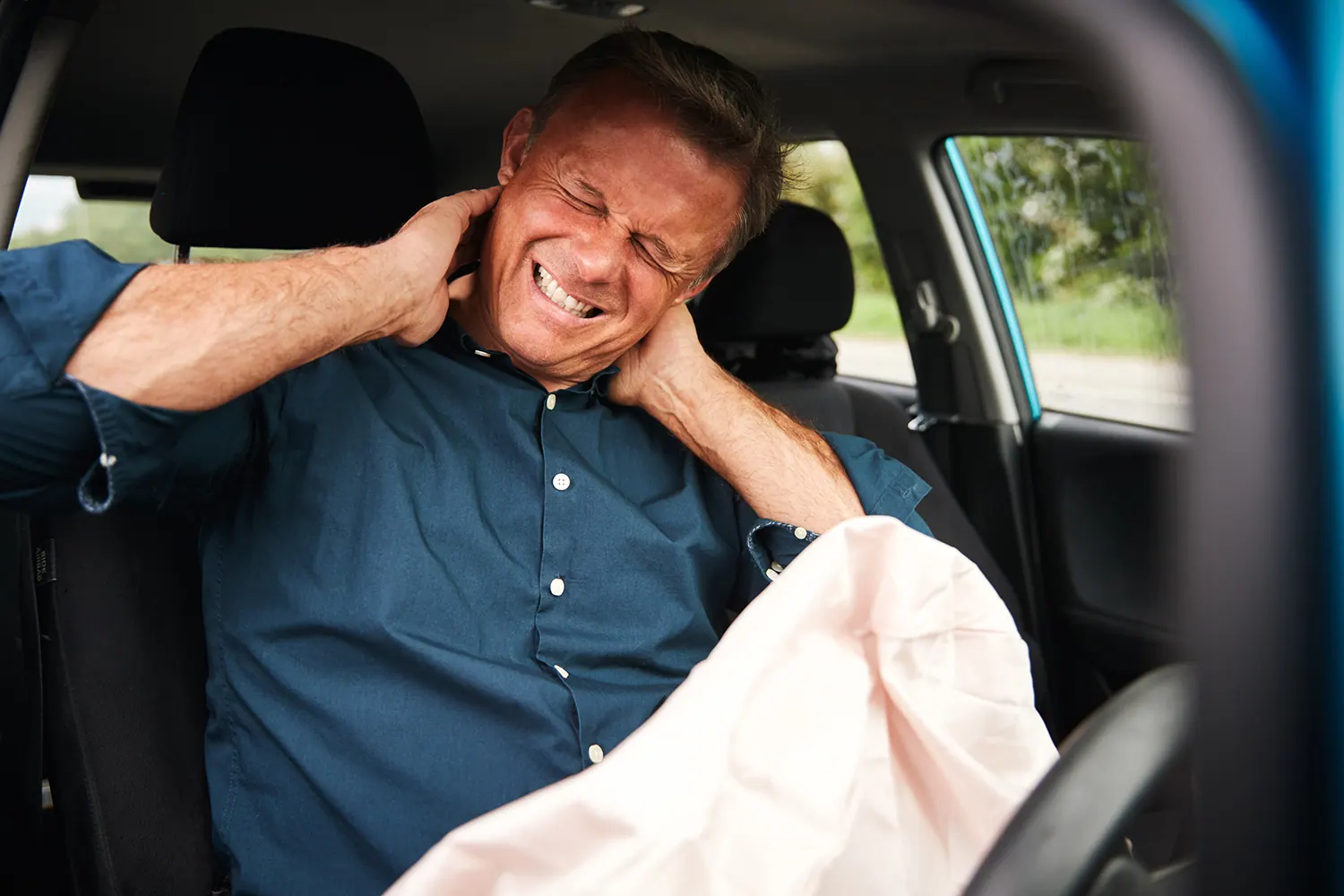 Man in a car holding his neck in pain beside a deployed airbag