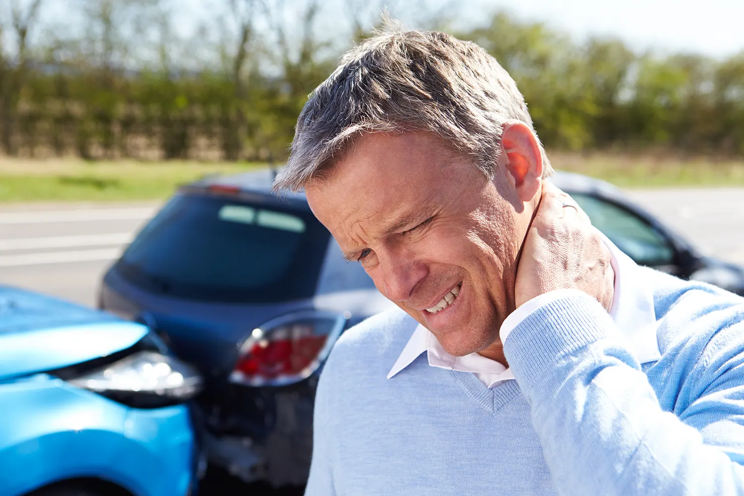 Man holding his neck in pain beside a car after an accident