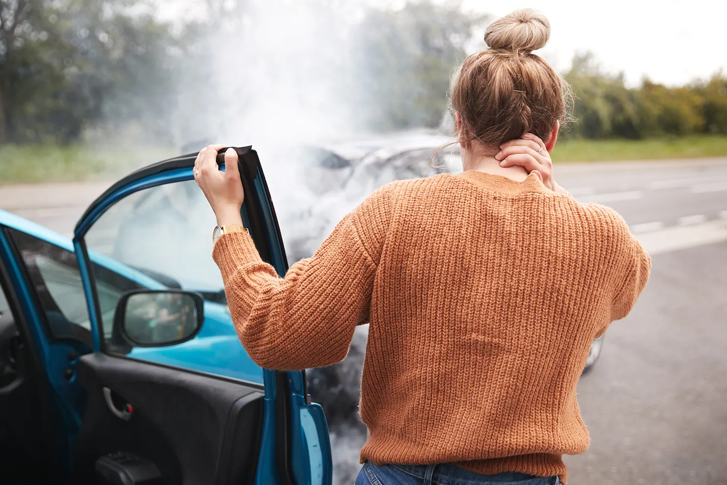 Woman holding her neck beside a car after a collision
