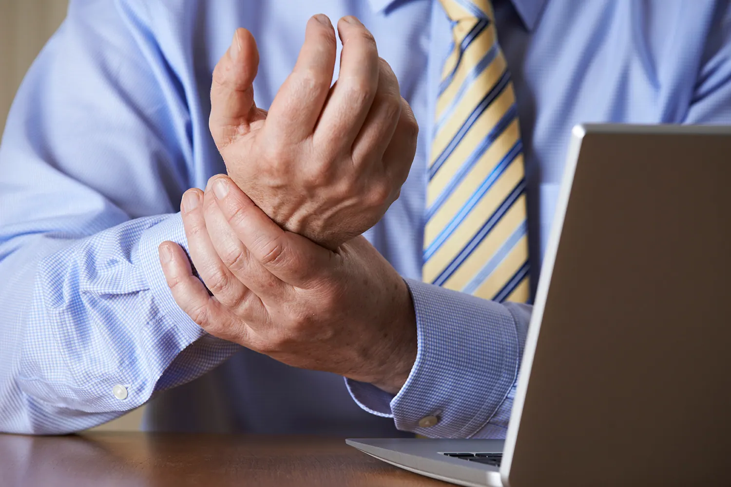 Man in a shirt and tie holding his wrist next to a laptop