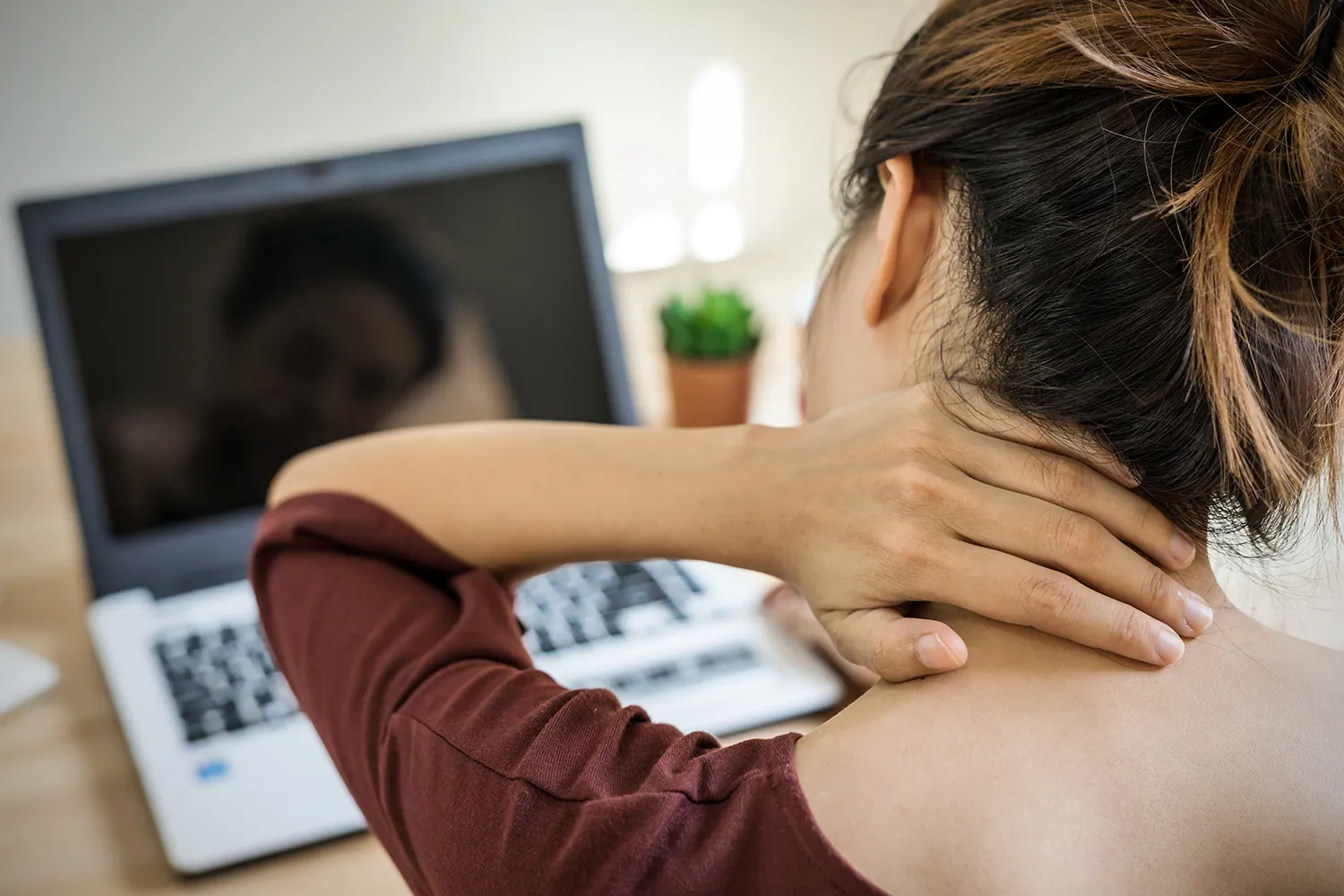 Woman at a laptop holding the back of her neck